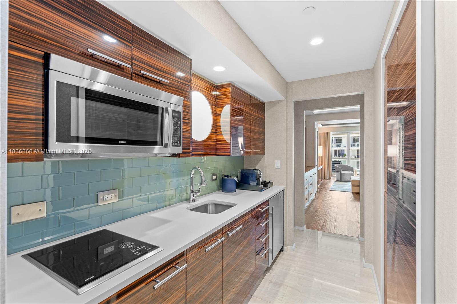 A modern kitchenette features wood-grain cabinets, a white countertop, a glass cooktop, and blue-green backsplash — 551 N Fort Lauderdale Beach Blvd # R1909, Fort Lauderdale FL 33304, FORT LAUDERDALE, FL