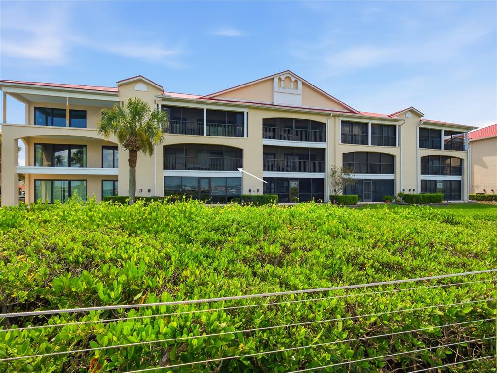A multi-story apartment building with screened balconies overlooks a large green hedge — 452 BOUCHELLE DRIVE UNIT 204, NEW SMYRNA BEACH, FL