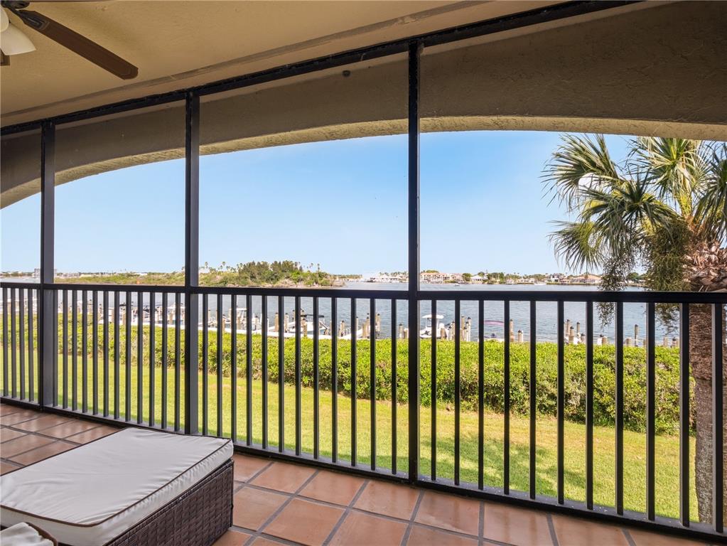 A screened-in balcony with tile flooring overlooks a grassy lawn, a boat dock, and water — 452 BOUCHELLE DRIVE UNIT 204, NEW SMYRNA BEACH, FL
