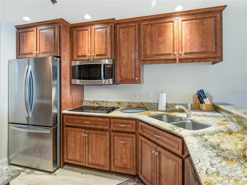 A kitchen features wood cabinets, stainless steel appliances, and granite countertops with a double sink — 452 BOUCHELLE DRIVE UNIT 204, NEW SMYRNA BEACH, FL