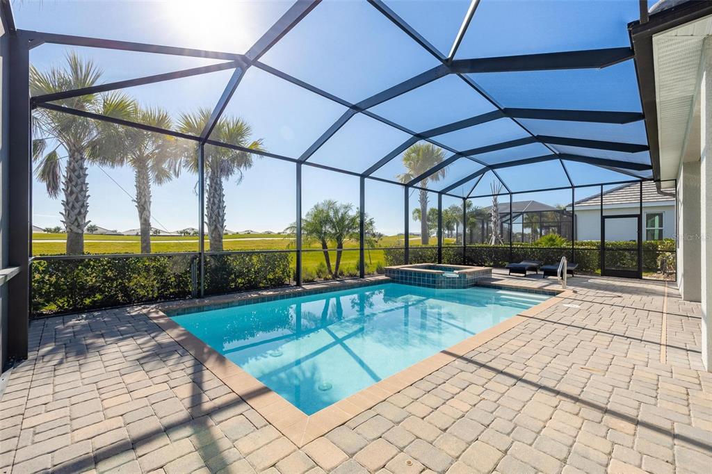 A screened-in patio features a rectangular swimming pool, a raised spa, and paver decking — 25199 LONGMEADOW DRIVE, PUNTA GORDA, FL