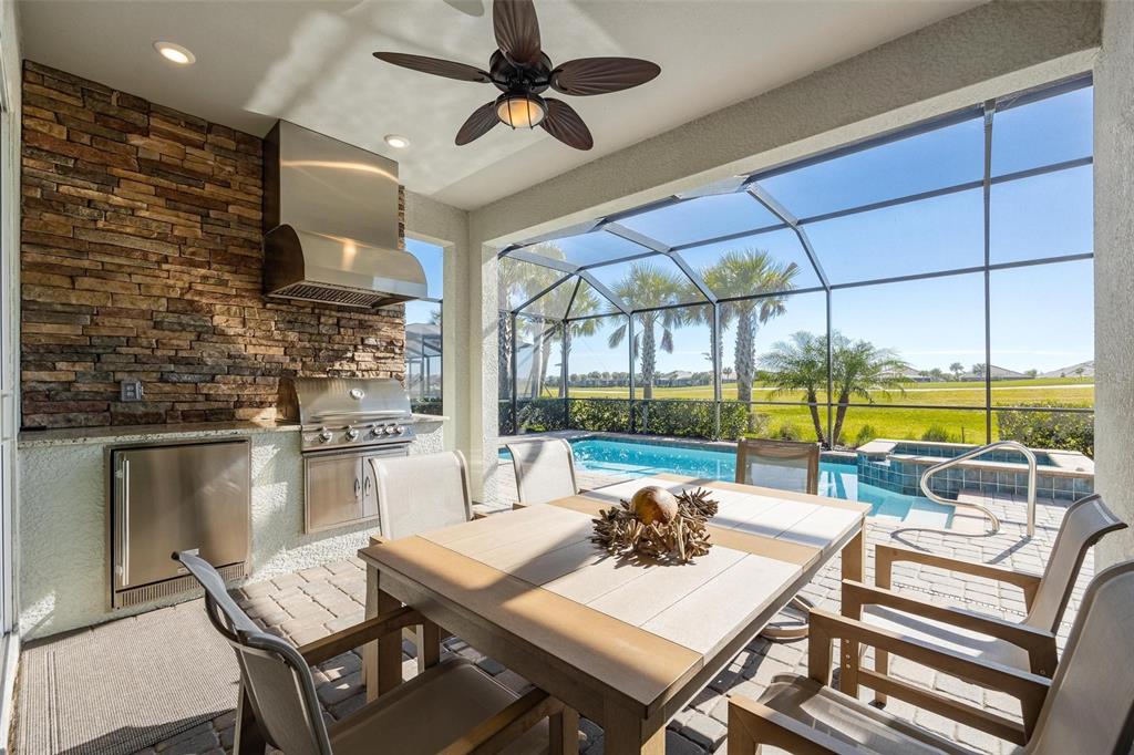 A covered outdoor patio features a stone-walled kitchen, dining set, and a screened-in swimming pool — 25199 LONGMEADOW DRIVE, PUNTA GORDA, FL