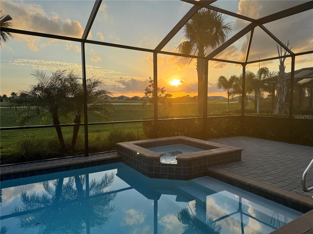 A screened-in pool and spa overlook a grassy landscape during a sunset — 25199 LONGMEADOW DRIVE, PUNTA GORDA, FL