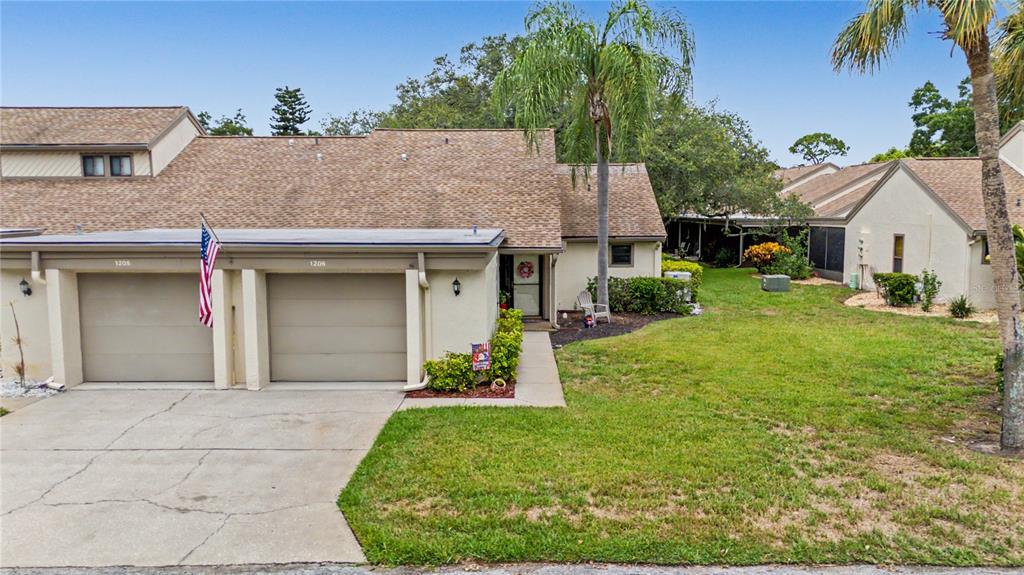 A tan townhouse with two garage doors, a front walkway, and a grassy lawn — 1206 PALM DRIVE, TARPON SPRINGS, FL
