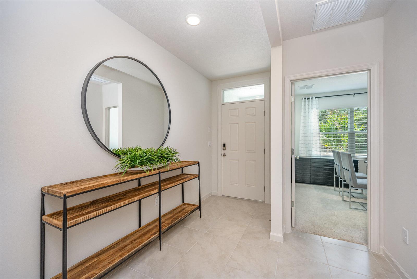 A bright entryway features a round mirror, a wooden console table, and tiled flooring — 721 SE Celtic Avenue, Port St. Lucie FL 34983, PORT ST. LUCIE, FL