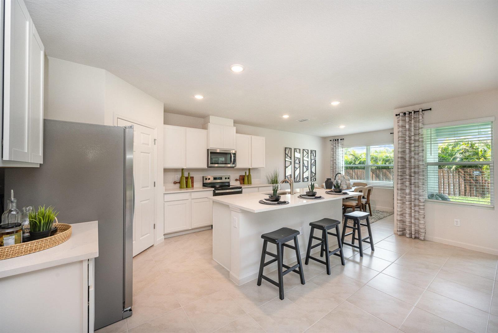 A bright kitchen features white cabinetry, a central island with bar stools, and tile flooring — 721 SE Celtic Avenue, Port St. Lucie FL 34983, PORT ST. LUCIE, FL