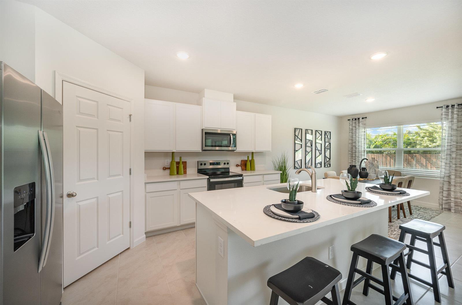 A bright kitchen features white cabinetry, stainless steel appliances, and a large central island — 721 SE Celtic Avenue, Port St. Lucie FL 34983, PORT ST. LUCIE, FL