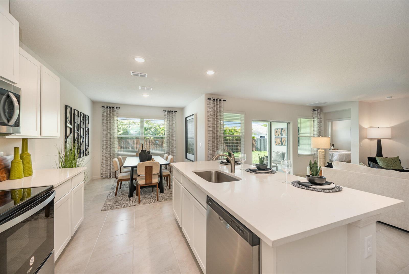 A modern kitchen with white cabinets and quartz countertops opens into a dining area — 721 SE Celtic Avenue, Port St. Lucie FL 34983, PORT ST. LUCIE, FL