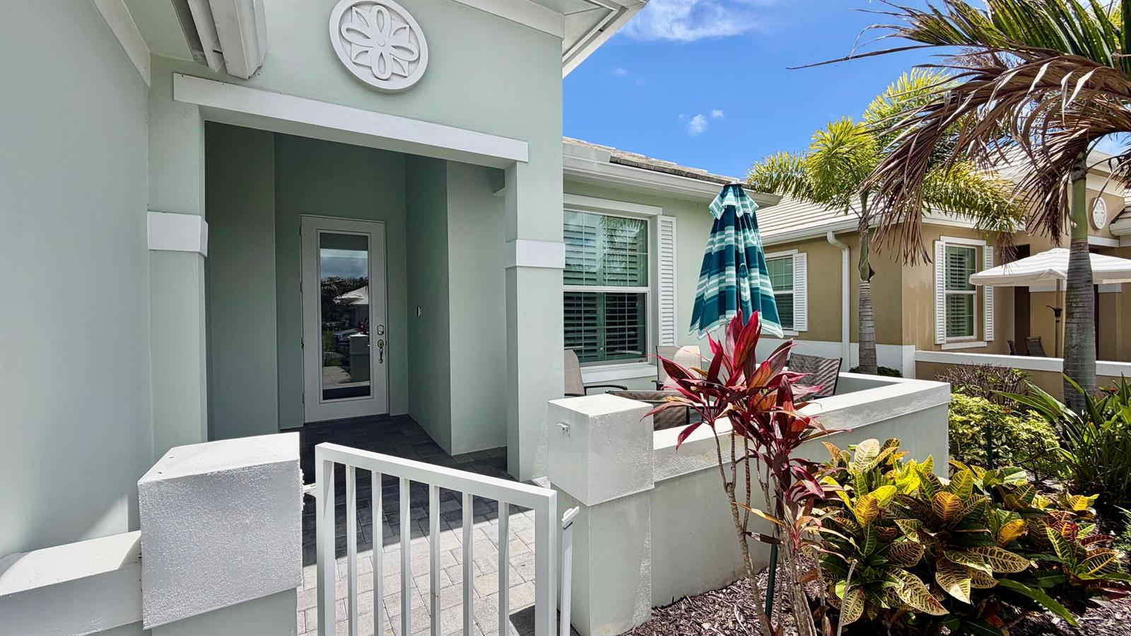 A light green house features a gated front courtyard with a patio and tropical landscaping — 1330 St Catherine's Circle, Vero Beach FL 32967, VERO BEACH, FL