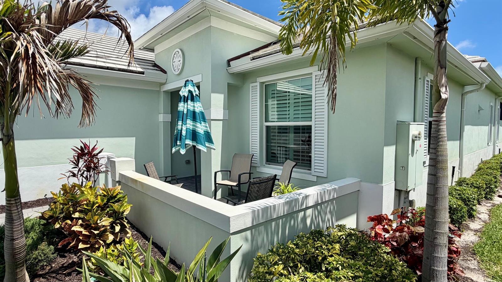 A light green house exterior features a small patio with chairs and a striped umbrella — 1330 St Catherine's Circle, Vero Beach FL 32967, VERO BEACH, FL