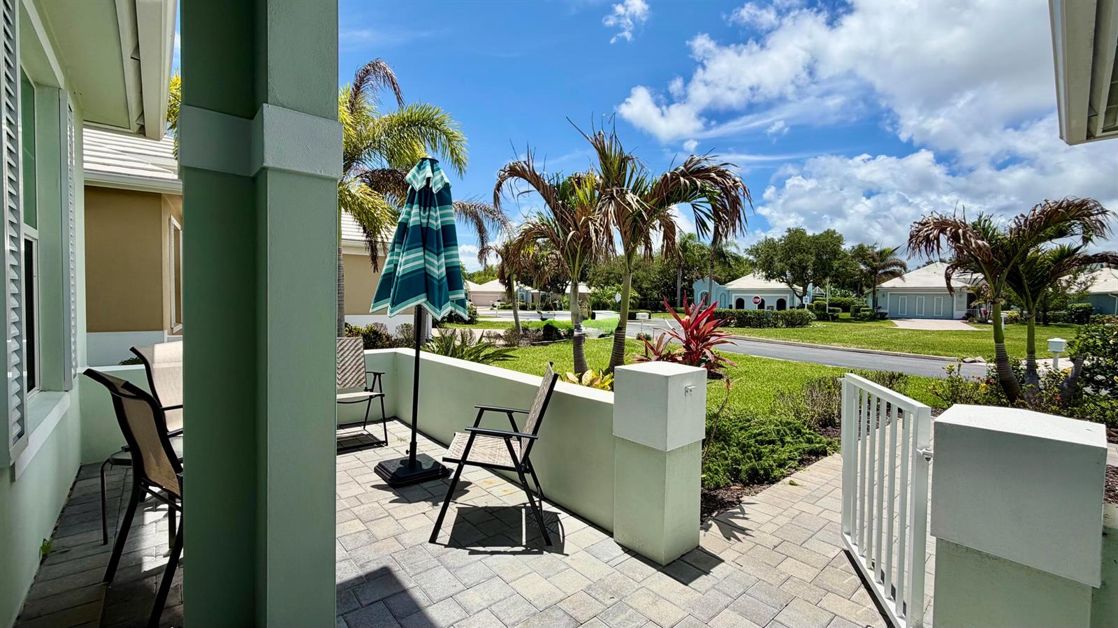A paved patio with outdoor chairs and a striped umbrella overlooks a suburban neighborhood street — 1330 St Catherine's Circle, Vero Beach FL 32967, VERO BEACH, FL