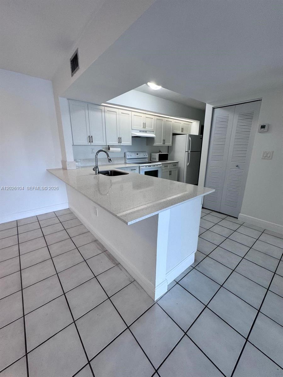 A kitchen features white cabinets, granite countertops, a breakfast bar, and light-colored tile flooring — 8600 SW 212th St # 308, Cutler Bay FL 33189, CUTLER BAY, FL