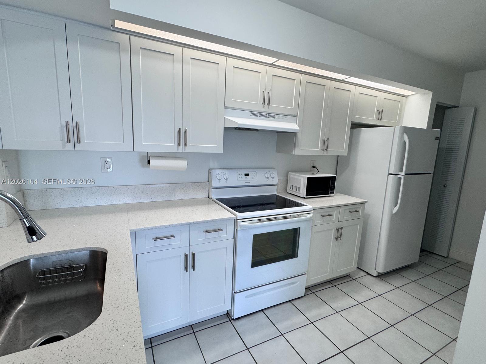 A kitchen features white cabinets, white appliances, and light-colored countertops with a tiled floor — 8600 SW 212th St # 308, Cutler Bay FL 33189, CUTLER BAY, FL