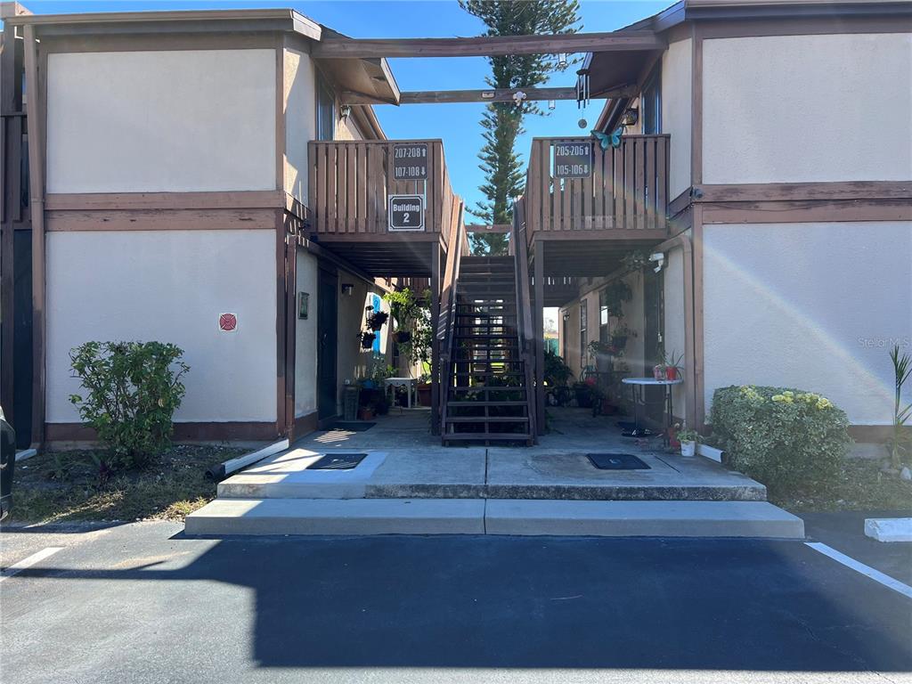 An exterior view of a two-story apartment building with a central staircase and wooden balconies — 5026 WATER OAK DRIVE UNIT 208, BRADENTON, FL