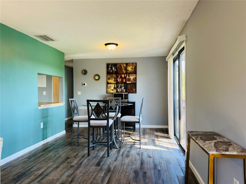 A dining area features a glass-top table, four chairs, wood-look flooring, and a teal accent wall — 5026 WATER OAK DRIVE UNIT 208, BRADENTON, FL