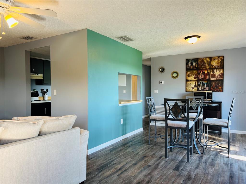 A living and dining area features wood-look flooring, a teal accent wall, and a pass-through window — 5026 WATER OAK DRIVE UNIT 208, BRADENTON, FL