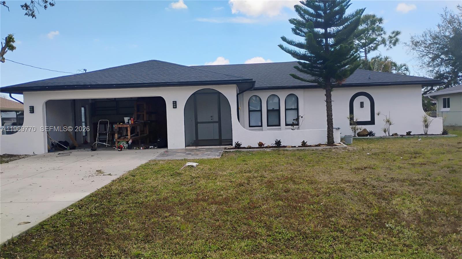 A single-story white house with a garage, arched entryway, and dark-framed windows — 1404 SE 19TH St., Cape Coral FL 33990, CAPE CORAL, FL