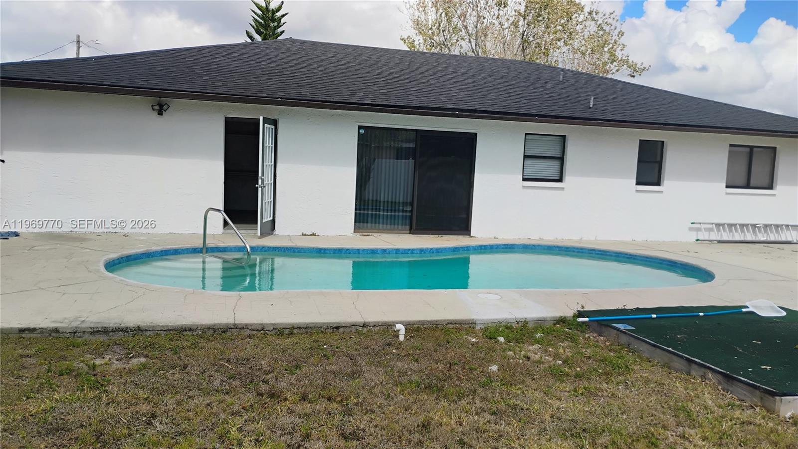 A white house with a dark roof features a swimming pool in the backyard — 1404 SE 19TH St., Cape Coral FL 33990, CAPE CORAL, FL