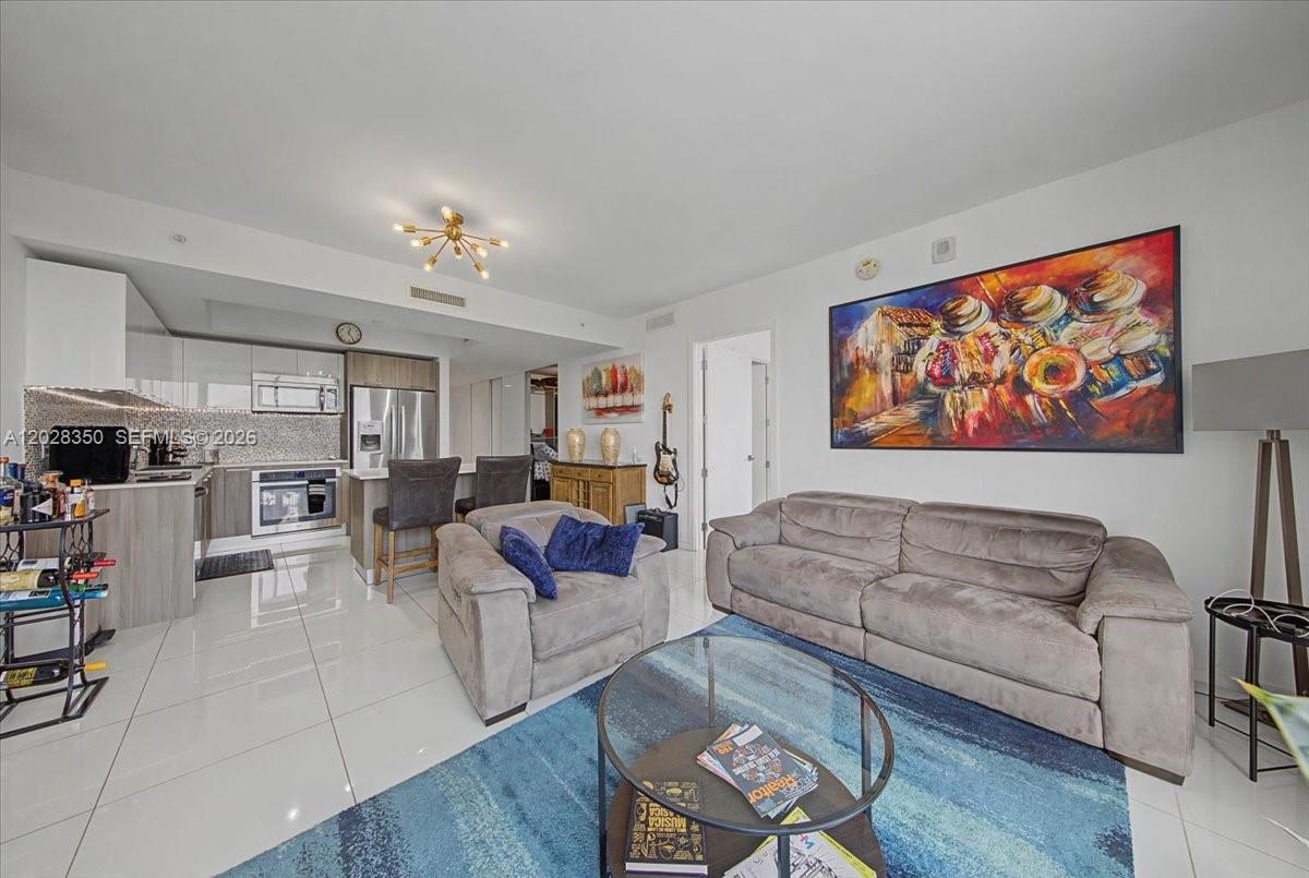A living room with a grey sofa, armchair, glass coffee table, and an open kitchen — 5252 NW 85th Ave # 1410, Doral FL 33166, DORAL, FL