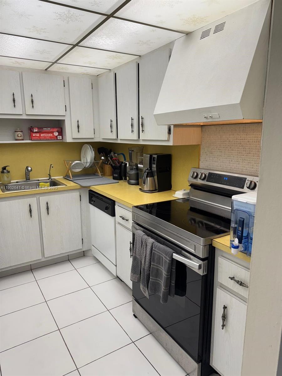 A kitchen features white cabinets, yellow countertops, a black stove, and white floor tiles — 500 Three Islands Blvd # 908, Hallandale Beach FL 33009, HALLANDALE BEACH, FL