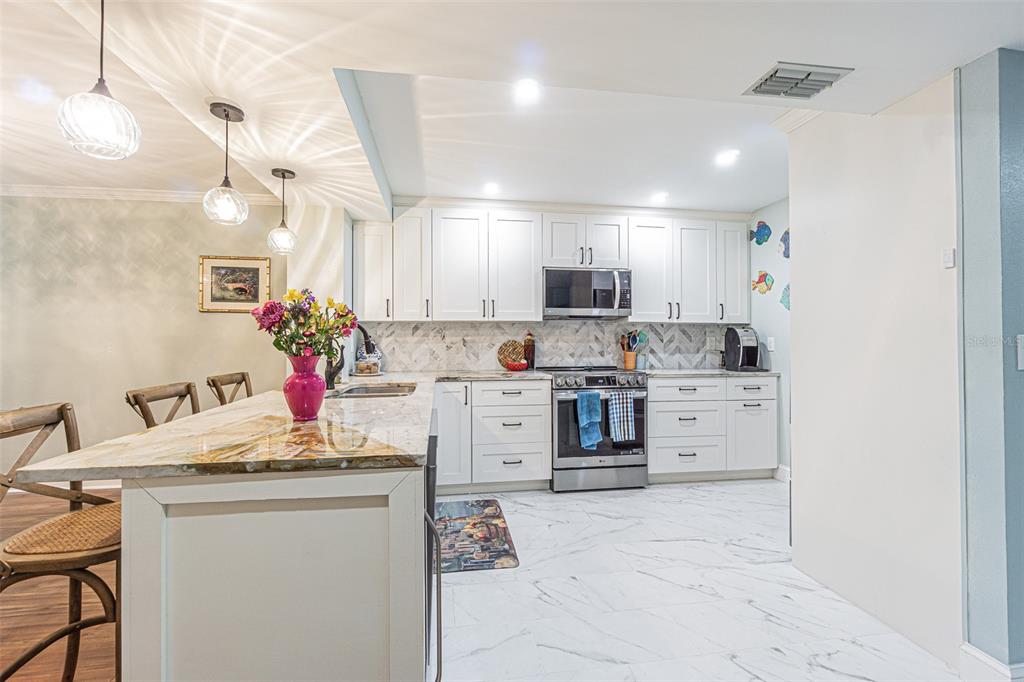 A kitchen features white cabinetry, stainless steel appliances, a marble-patterned island, and white tile flooring — 3505 TARPON WOODS BOULEVARD UNIT G405, PALM HARBOR, FL