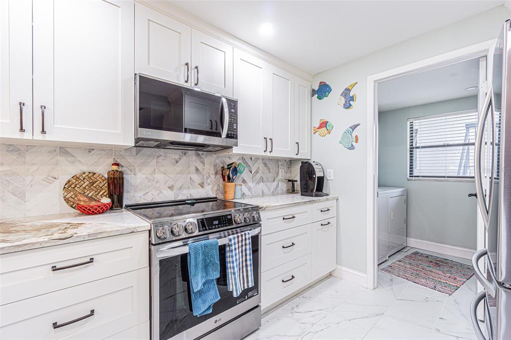 A kitchen features white cabinets, stainless steel appliances, marble-style backsplash, and a laundry room doorway — 3505 TARPON WOODS BOULEVARD UNIT G405, PALM HARBOR, FL