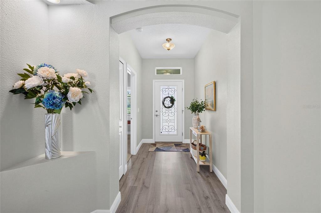A bright entryway features an arched ceiling, light wood-look flooring, and a glass-paneled front door — 55 HUNTINGTON PLACE, ORMOND BEACH, FL