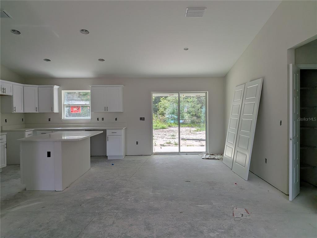 An unfinished kitchen and living area features white cabinets, a center island, and sliding glass doors — 8943 N TROJAN DRIVE S, CITRUS SPRINGS, FL