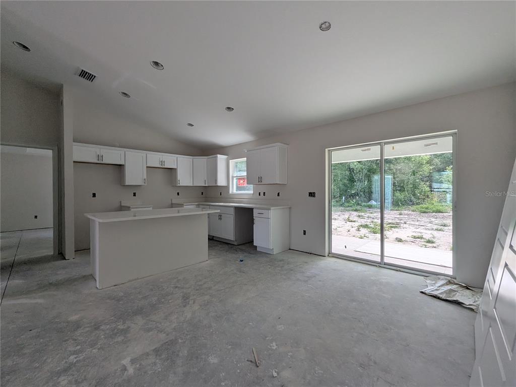 An unfinished kitchen features white cabinets, a central island, and sliding glass doors to outdoors — 8943 N TROJAN DRIVE S, CITRUS SPRINGS, FL