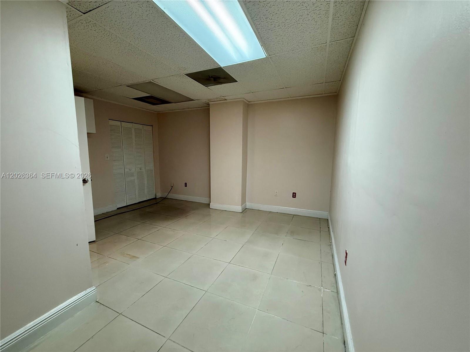 An empty room features light-colored tile flooring, a drop ceiling with recessed lighting, and closet doors — 8370 W Flagler St # 120, Miami FL 33144, MIAMI, FL