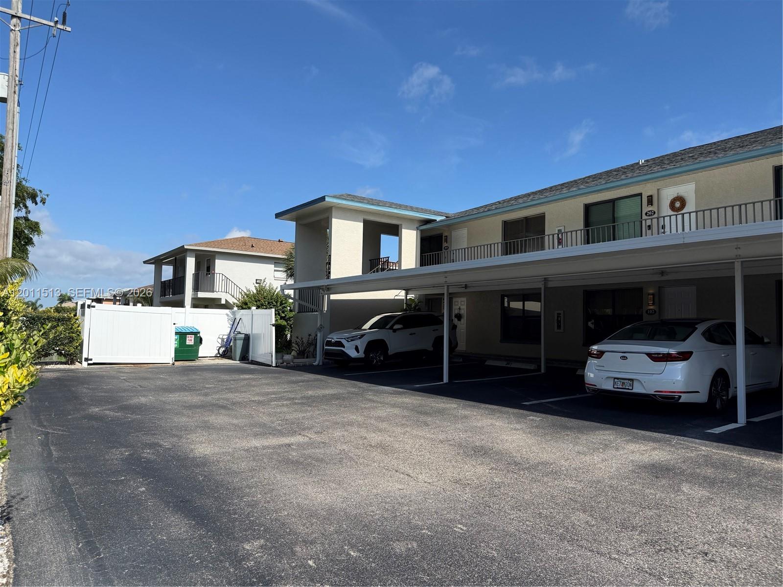 A two-story apartment building features a covered parking area with two white cars parked underneath — 123 SW 47TH TER # 201, Cape Coral FL 33914, CAPE CORAL, FL