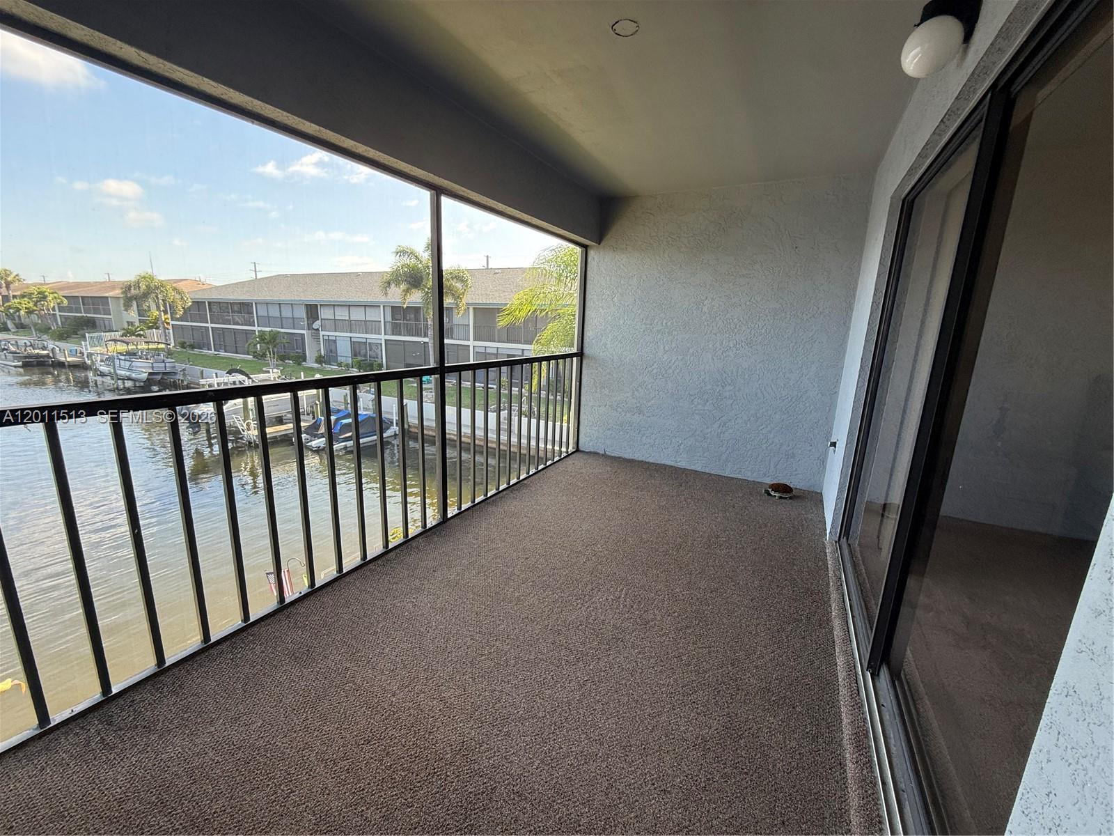 A balcony with brown carpeting overlooks a canal with docked boats and apartment buildings — 123 SW 47TH TER # 201, Cape Coral FL 33914, CAPE CORAL, FL