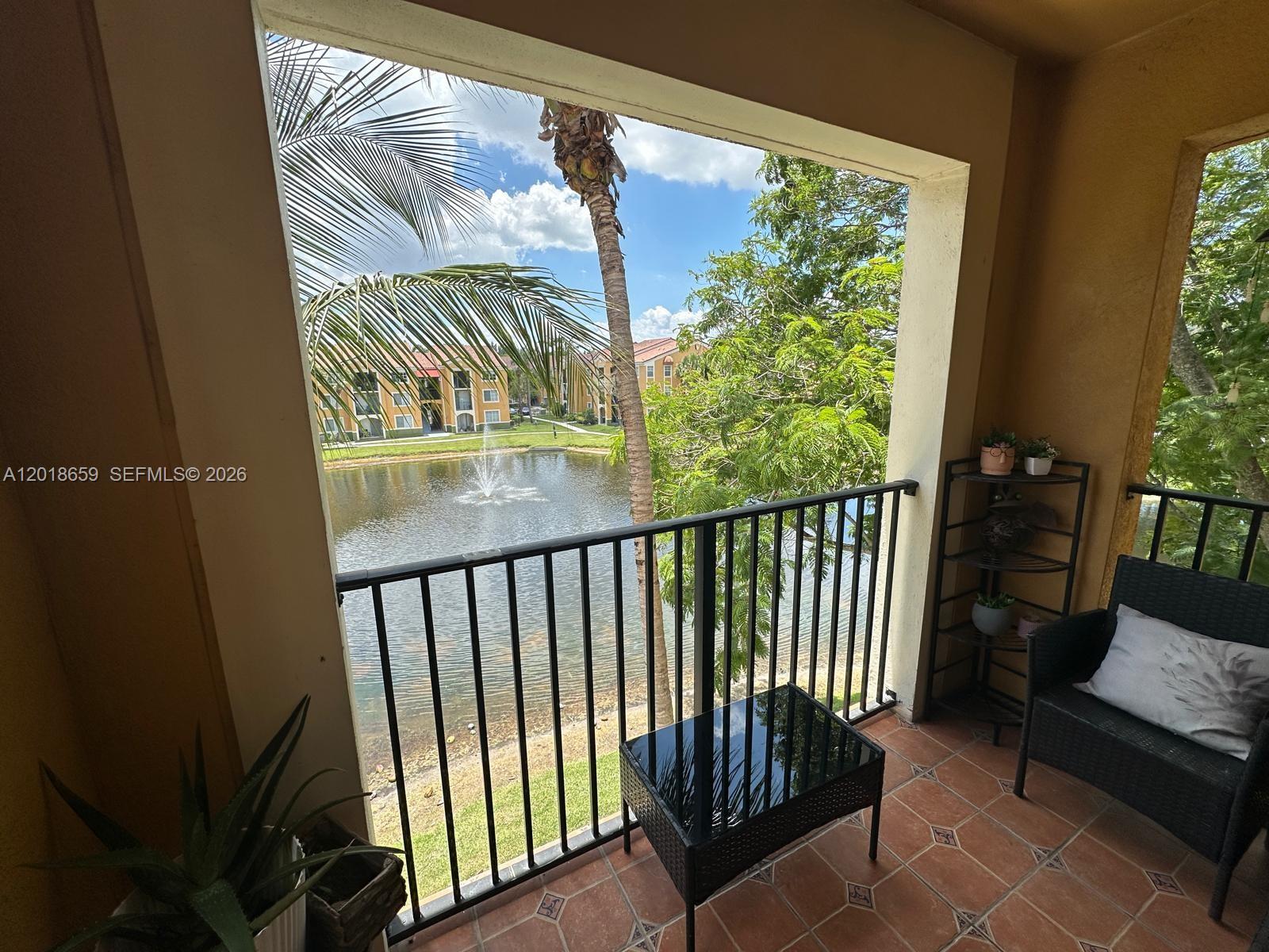A balcony with tile flooring overlooks a lake with a fountain and palm trees — 2240 E Preserve Way # 308, Miramar FL 33025, MIRAMAR, FL