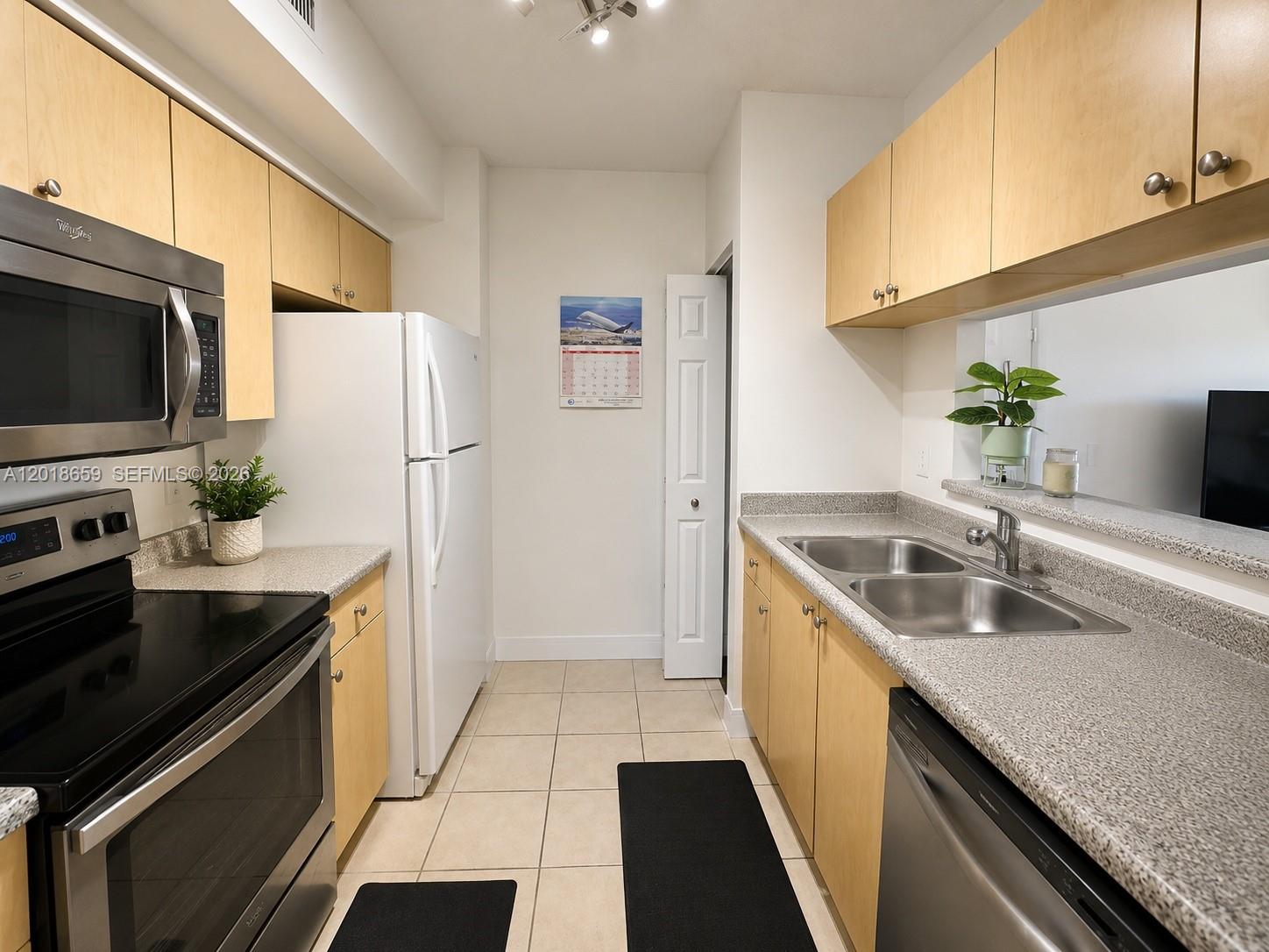 A galley kitchen features light wood cabinets, granite countertops, stainless steel appliances, and tile flooring — 2240 E Preserve Way # 308, Miramar FL 33025, MIRAMAR, FL