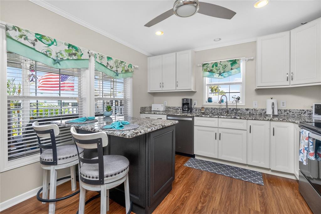A kitchen features white cabinets, granite countertops, a dark island with bar stools, and wood flooring — 10303 BURNT STORE ROAD UNIT 233, PUNTA GORDA, FL