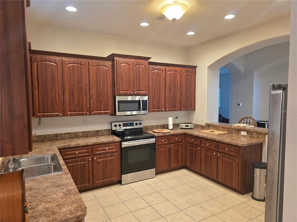 A kitchen features dark wood cabinets, laminate countertops, stainless steel appliances, and tile flooring — 4266 HIGH RIDGE AVENUE, SPRING HILL, FL