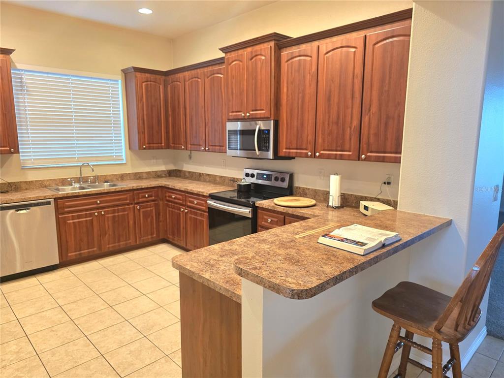 A kitchen with wood cabinets, laminate countertops, stainless steel appliances, and a breakfast bar — 4266 HIGH RIDGE AVENUE, SPRING HILL, FL