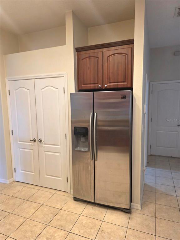 A stainless steel refrigerator sits beneath wooden cabinets next to a white double-door closet — 4266 HIGH RIDGE AVENUE, SPRING HILL, FL