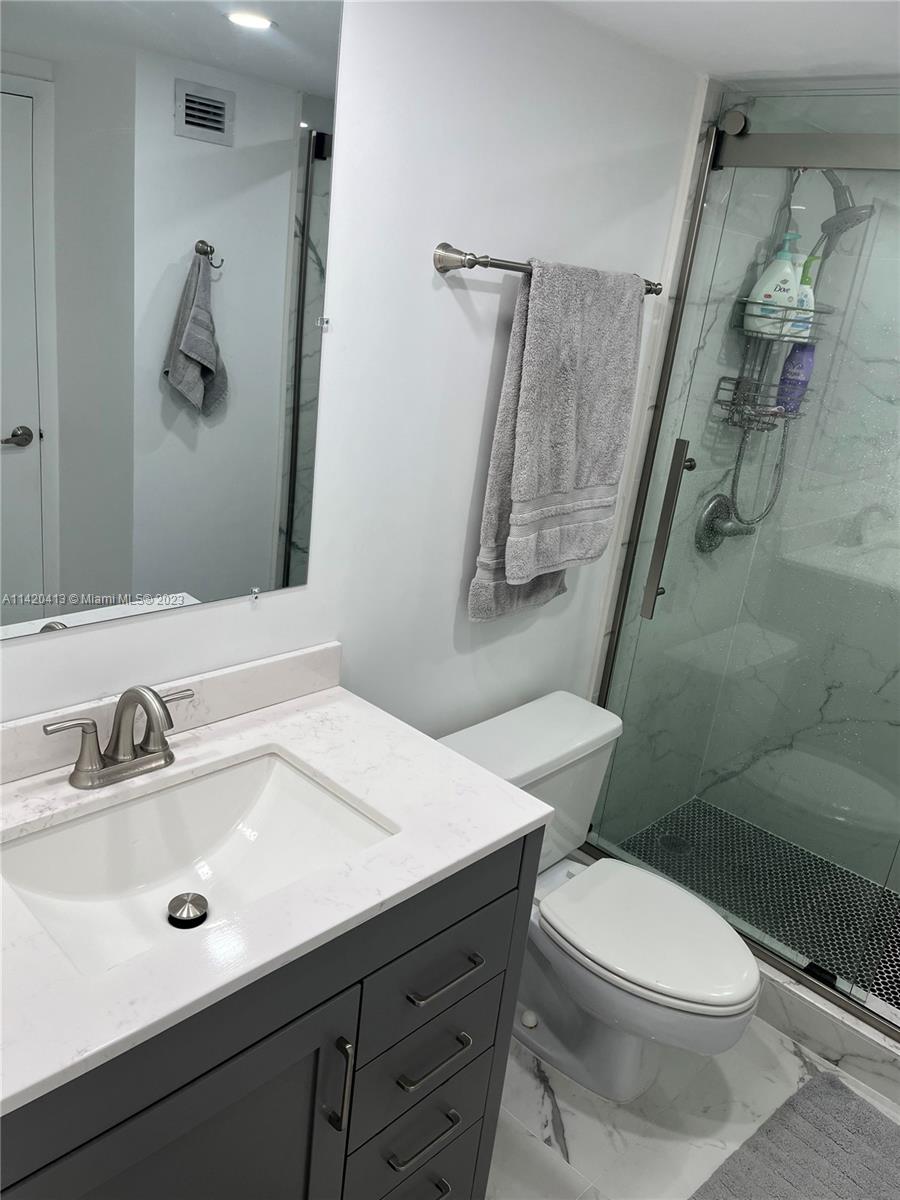 A bathroom features a gray vanity, white countertop, toilet, and a glass-enclosed walk-in shower — 2030 S Ocean Dr # 1602, Hallandale Beach FL 33009, HALLANDALE BEACH, FL