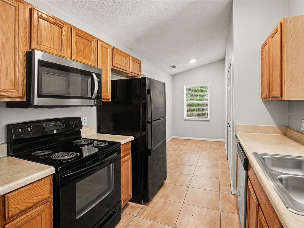 A kitchen features wood cabinets, black appliances, tile flooring, and a vaulted ceiling — 2481 WINCHESTER BOULEVARD, KISSIMMEE, FL