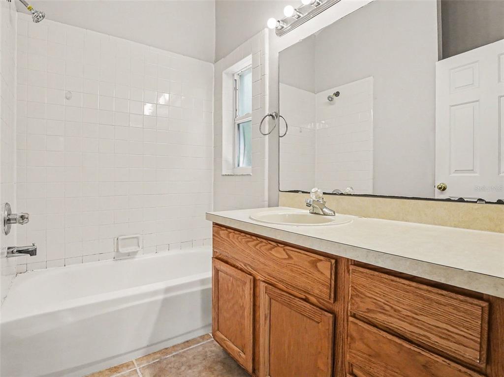 A bathroom features a white tiled shower-tub combo, a wooden vanity, and a large mirror — 2481 WINCHESTER BOULEVARD, KISSIMMEE, FL