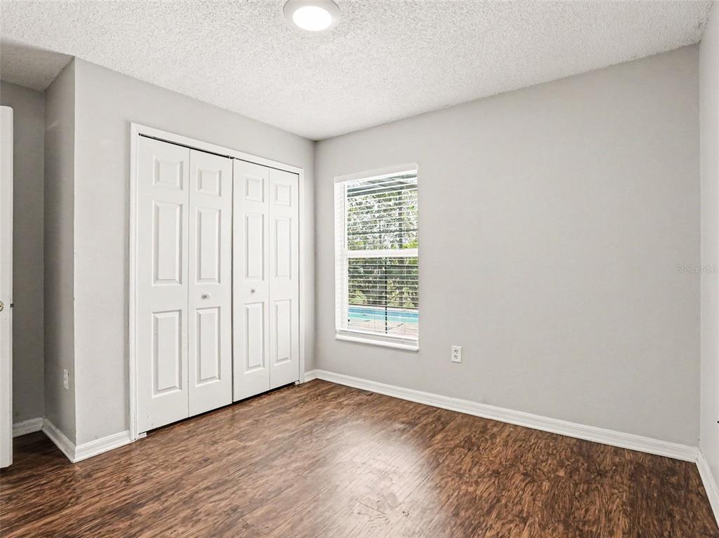 A bedroom with gray walls, wood-look flooring, white bi-fold closet doors, and a single window — 2481 WINCHESTER BOULEVARD, KISSIMMEE, FL