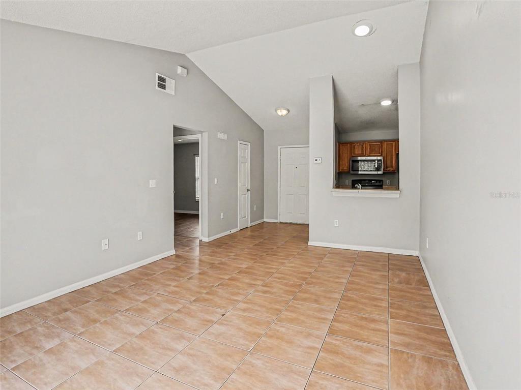 An open-concept living area features vaulted ceilings, light-colored walls, and tan tiled flooring — 2481 WINCHESTER BOULEVARD, KISSIMMEE, FL
