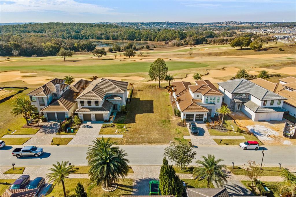 An aerial view shows two houses flanking a vacant lot overlooking a golf course — 15938 VETTA DRIVE, BELLA COLLINA, FL