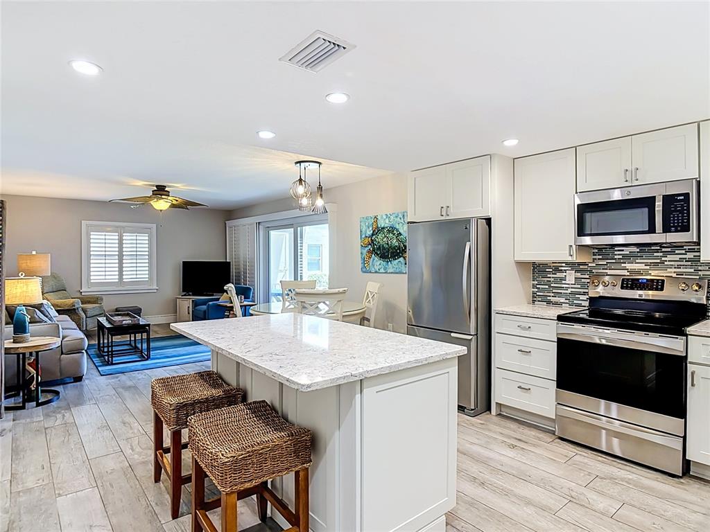 An open-concept kitchen and living area features a stone-topped island, stainless appliances, and tile flooring — 4495 S ATLANTIC AVENUE UNIT 1010, NEW SMYRNA BEACH, FL