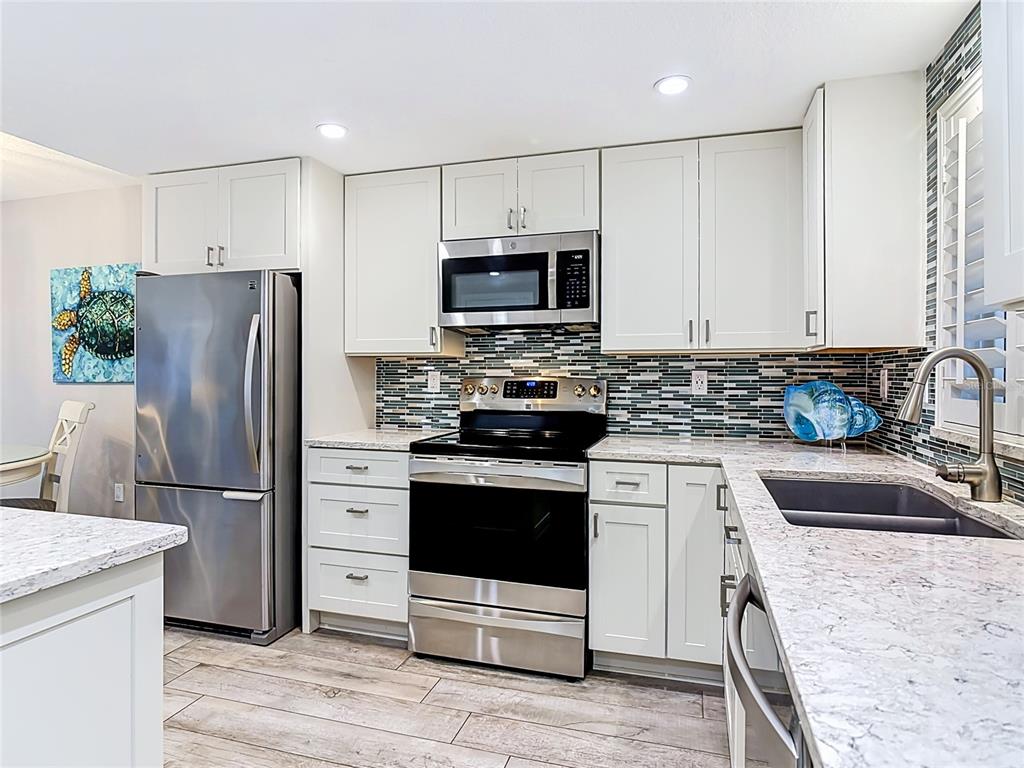 A kitchen features white cabinets, stainless steel appliances, granite countertops, and a mosaic tile backsplash — 4495 S ATLANTIC AVENUE UNIT 1010, NEW SMYRNA BEACH, FL