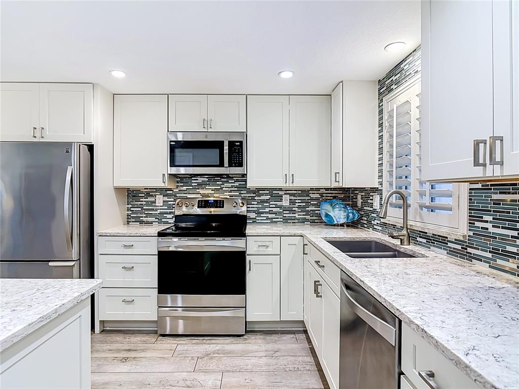 A kitchen with white cabinets, stainless steel appliances, granite countertops, and a blue tile backsplash — 4495 S ATLANTIC AVENUE UNIT 1010, NEW SMYRNA BEACH, FL