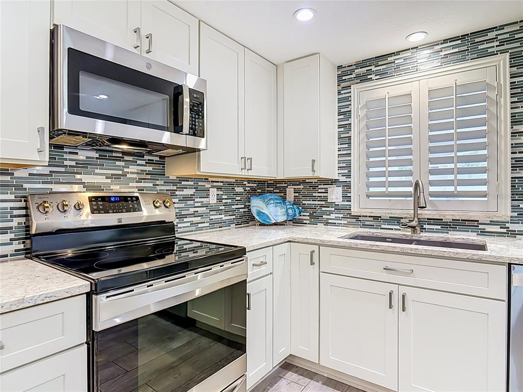 A kitchen features white cabinets, stainless steel appliances, a patterned backsplash, and a corner sink — 4495 S ATLANTIC AVENUE UNIT 1010, NEW SMYRNA BEACH, FL