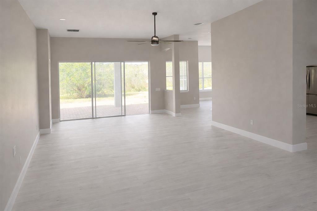 An open-concept living area features light wood-look flooring, neutral walls, and sliding glass patio doors — 3504 VALLEYVIEW DRIVE, KISSIMMEE, FL