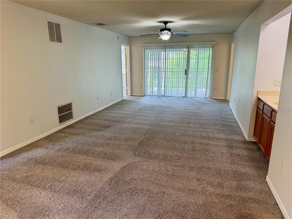 An empty living room features gray carpeting, a ceiling fan, and sliding glass balcony doors — 4316 CLUBSIDE DRIVE UNIT 4316, LONGWOOD, FL